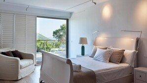 Ein modernes Schlafzimmer mit einem großen Bett, einem Sessel, einem Nachttisch und Blick ins Freie.