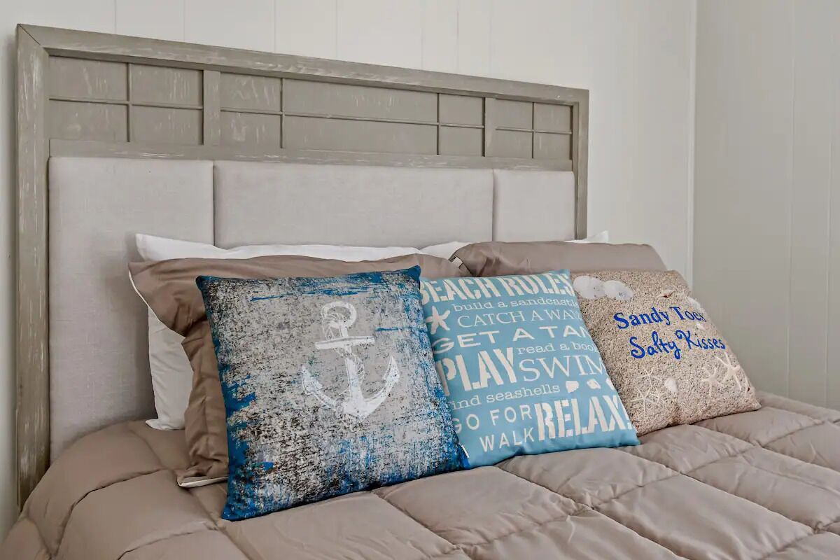 A bed with a headboard and three decorative pillows with nautical themes.