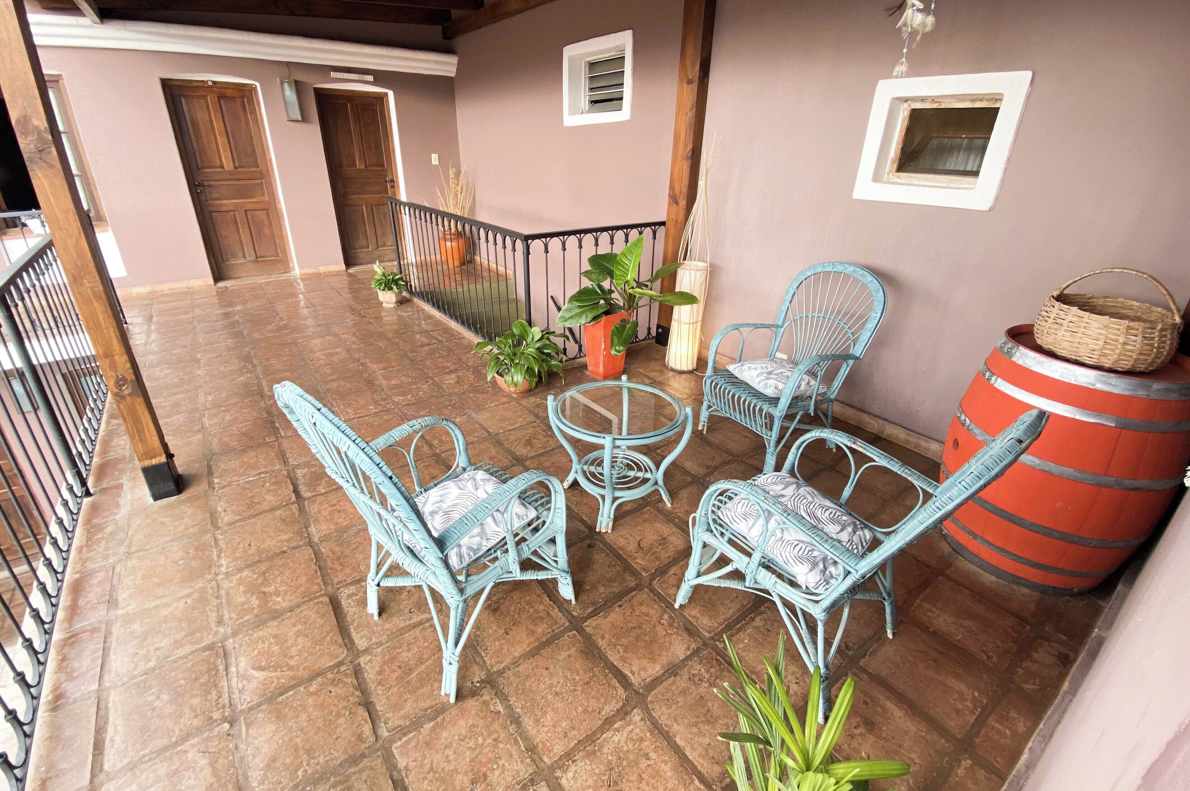 Ein überdachter Patio-Bereich mit Korbmöbeln, Topfpflanzen und einem großen Fass.