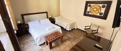 A hotel room with a large bed, a smaller bed, a wooden bench, a desk, and a chair.