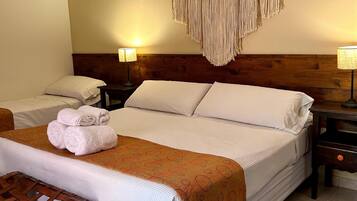 A hotel room with a large bed, two bedside tables, a wooden headboard, a macrame wall hanging, and a woven basket.