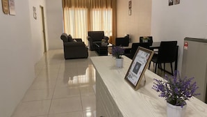 A modern living room with a sofa, a coffee table, and a dining area with chairs. There is a refrigerator and a ceiling fan. - Hotel O Bayu Service Apartment (Langkawi)