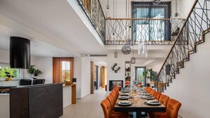 Una cocina moderna con una isla central, un comedor con sillas tapizadas en naranja, y una escalera con barandilla geométrica.