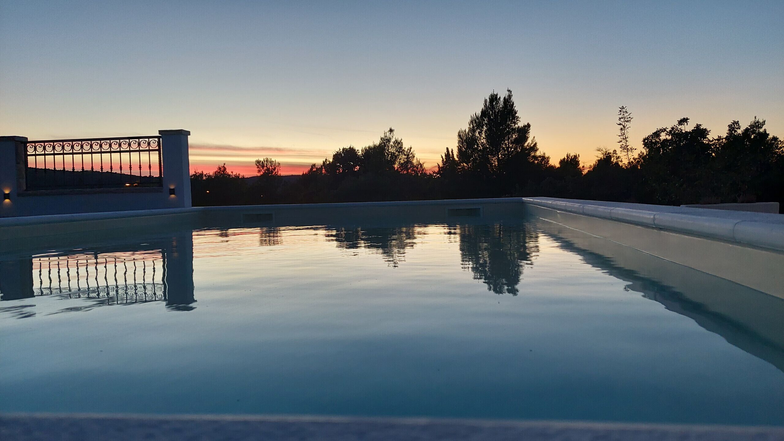A swimming pool with a clear view of the sunset and surrounding trees.