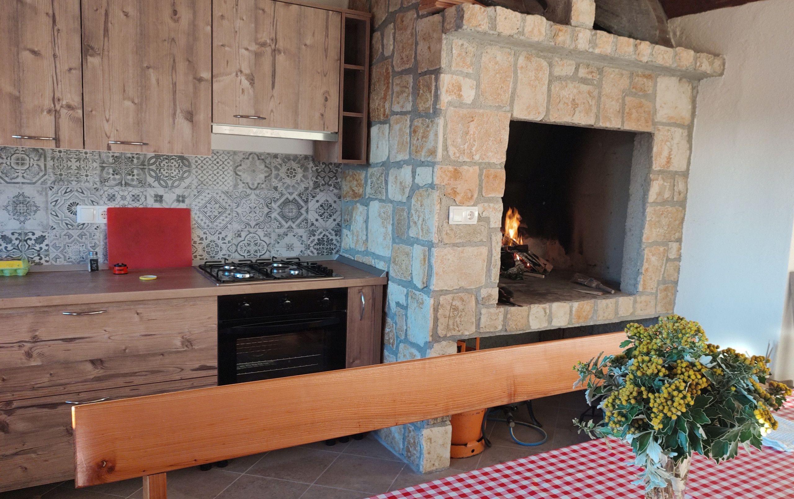 Una cucina con camino in pietra, pensili in legno e tovaglia rossa.