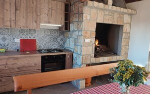 A kitchen with a stone fireplace, wooden cabinets, and a red tablecloth.