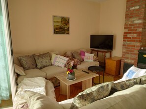A cozy living room with a sofa, a coffee table with flowers, a television, and a brick wall.