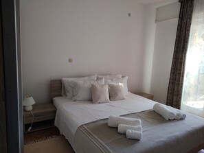 Ein ordentlich bezogenes Bett mit weißen Leinen und Kissen, eine Nachttischlampe und ein Fenster mit Vorhängen.