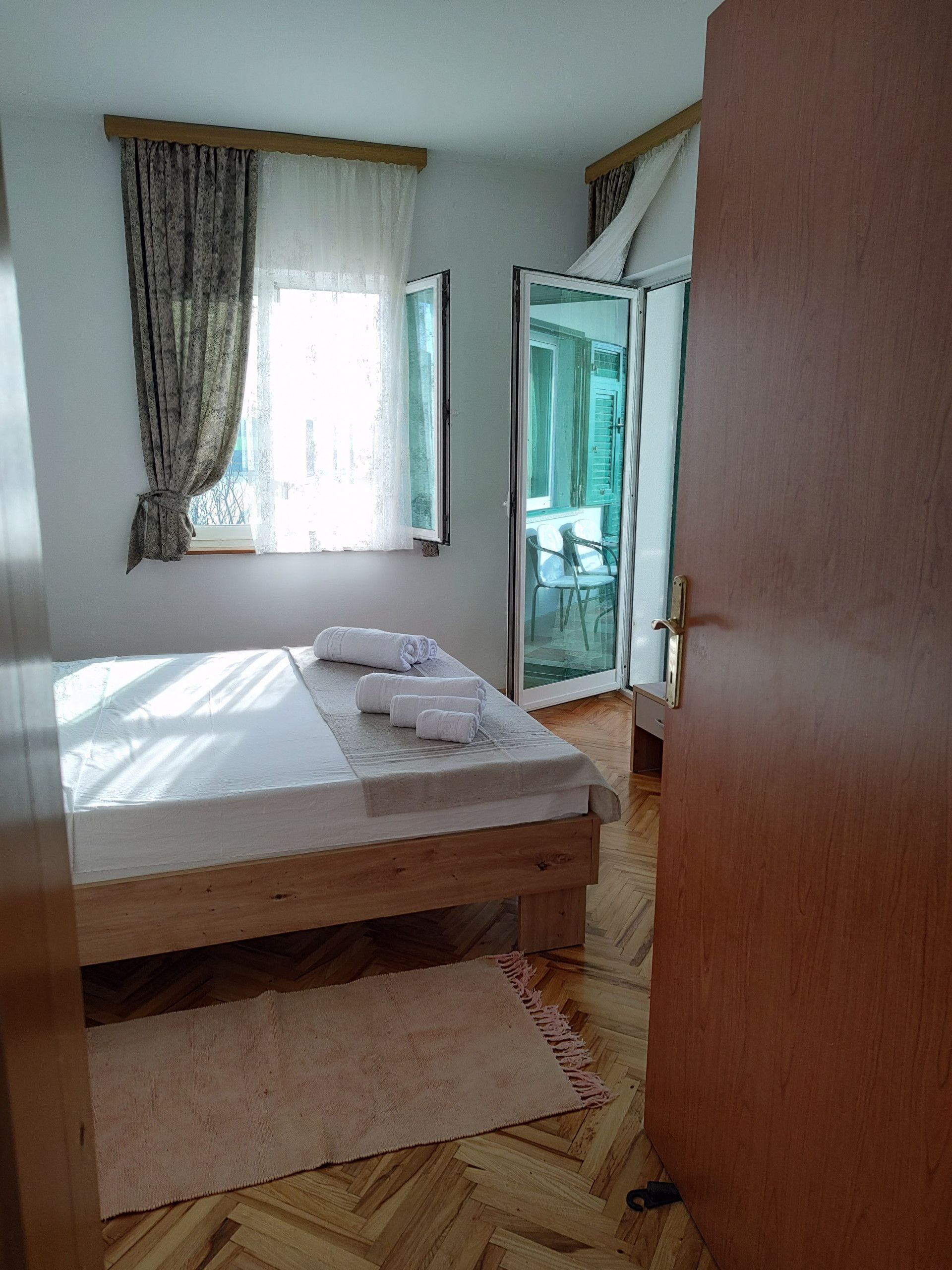 Een slaapkamer met een houten bed, een raam met gordijnen, uitzicht op de omgeving en een schuifdeur met glas.