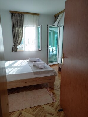 A bedroom with a wooden bed, a window with curtains, a view of the outside, and a sliding glass door. - Apartment Lemi - three bedroom apartment with a sea view (Ražanac)