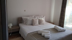 Ein ordentlich bezogenes Bett mit weißen Leinen und Kissen, eine Nachttischlampe und ein Fenster mit Vorhängen.