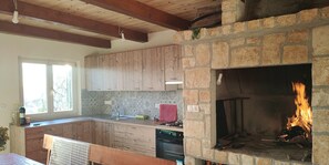 A kitchen with wooden cabinets, a stone fireplace, and a window with natural light. - Apartment Lemi - three bedroom apartment with a sea view (Ražanac)