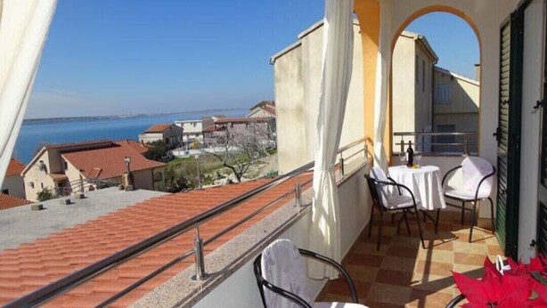 Ein Balkon mit Meerblick, zwei Tische mit Stühlen und ein Blumentopf.