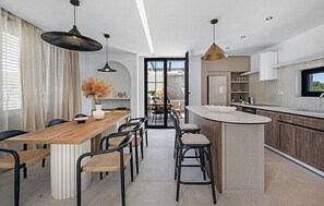 A modern kitchen with a central island, bar stools, pendant lighting, and a view through an open door. - Villa Marantik - with outdoor pool (Bilice)