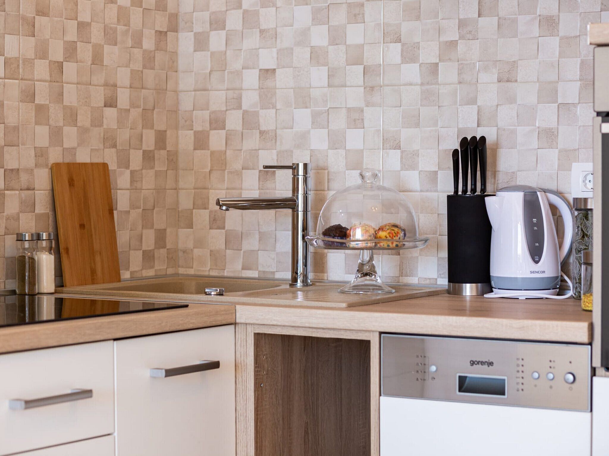 Eine moderne Küche mit kariertem Fliesenrückwand, einer Edelstahl-Spüle, einer Kaffeemaschine und einem Geschirrspüler.