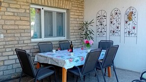 An outdoor dining area with a table set for four, surrounded by chairs, against a stone wall. - Apartments Alaga - C (Tribunj)