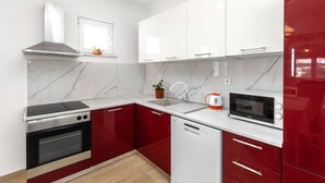 A modern kitchen with red and white cabinetry, a built-in oven, a microwave, and a window above the sink. - Apartments Alaga - C (Tribunj)