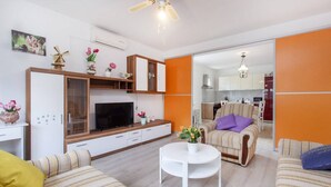 A modern living room with a sofa, a coffee table, and a TV. There is a kitchen visible through an open door. - Apartments Alaga - C (Tribunj)