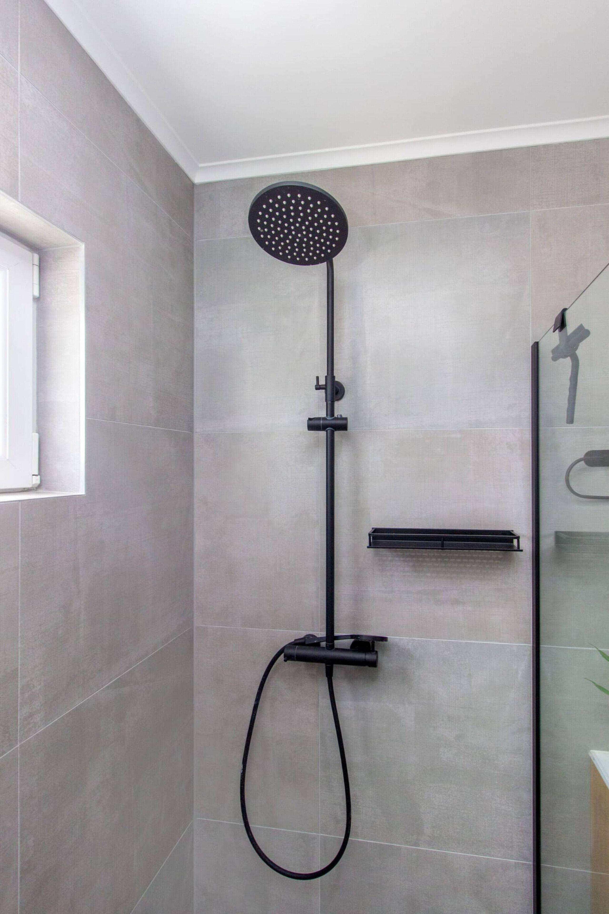 A modern shower with a round head, a handheld showerhead, and a control panel.