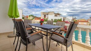 A balcony with a table and chairs, a green umbrella, and a view of buildings. - Apartments Alaga - A1 (Tribunj)
