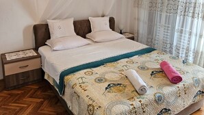 Ein ordentlich bezogenes Bett mit einem gemusterten Überwurf, einem weißen Moskitonetz und einem hölzernen Nachttisch mit einer Schublade.