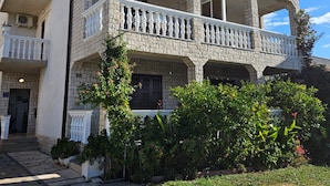 Un bâtiment à deux étages doté d’une façade en pierre, de balcons avec des balustrades blanches et d’un espace d’entrée pavé agrémenté de plantes en pot.