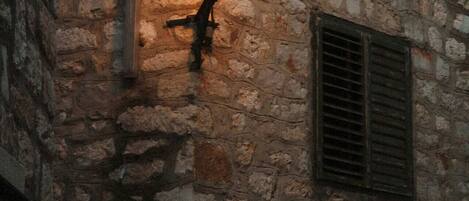 A stone wall with a hanging lantern and a shuttered window.