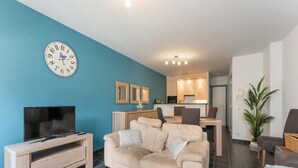 A modern living room with a sofa, a TV, and a dining area with chairs and a table. - Apartment in Blankenberge Near Belgium Pier (Blankenberge)