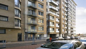 A multi-story residential building with balconies, a brick facade, and a parking area with cars. - Apartment in Blankenberge Near Belgium Pier (Blankenberge)