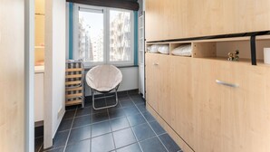 A compact room with a large wardrobe, a window with a view of buildings, a chair, and a small shelf with items. - Apartment in Blankenberge Near Belgium Pier (Blankenberge)