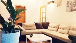 Una sala de estar con un sofá seccional color beige, una mesa de centro blanca y una planta grande en maceta.