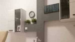 Una sala moderna con un mueble blanco para equipos electrónicos, un reloj y una planta pequeña.