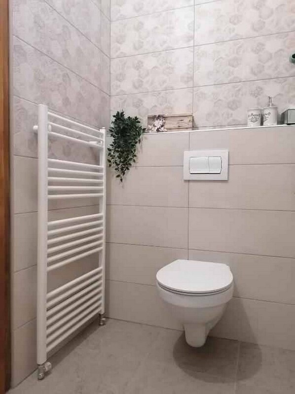 Un baño con un radiador blanco, un inodoro y un estante pequeño con artículos de aseo.