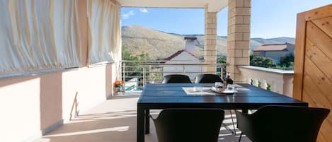 A balcony with a table and chairs, a view of a mountain, and a building with a red roof.