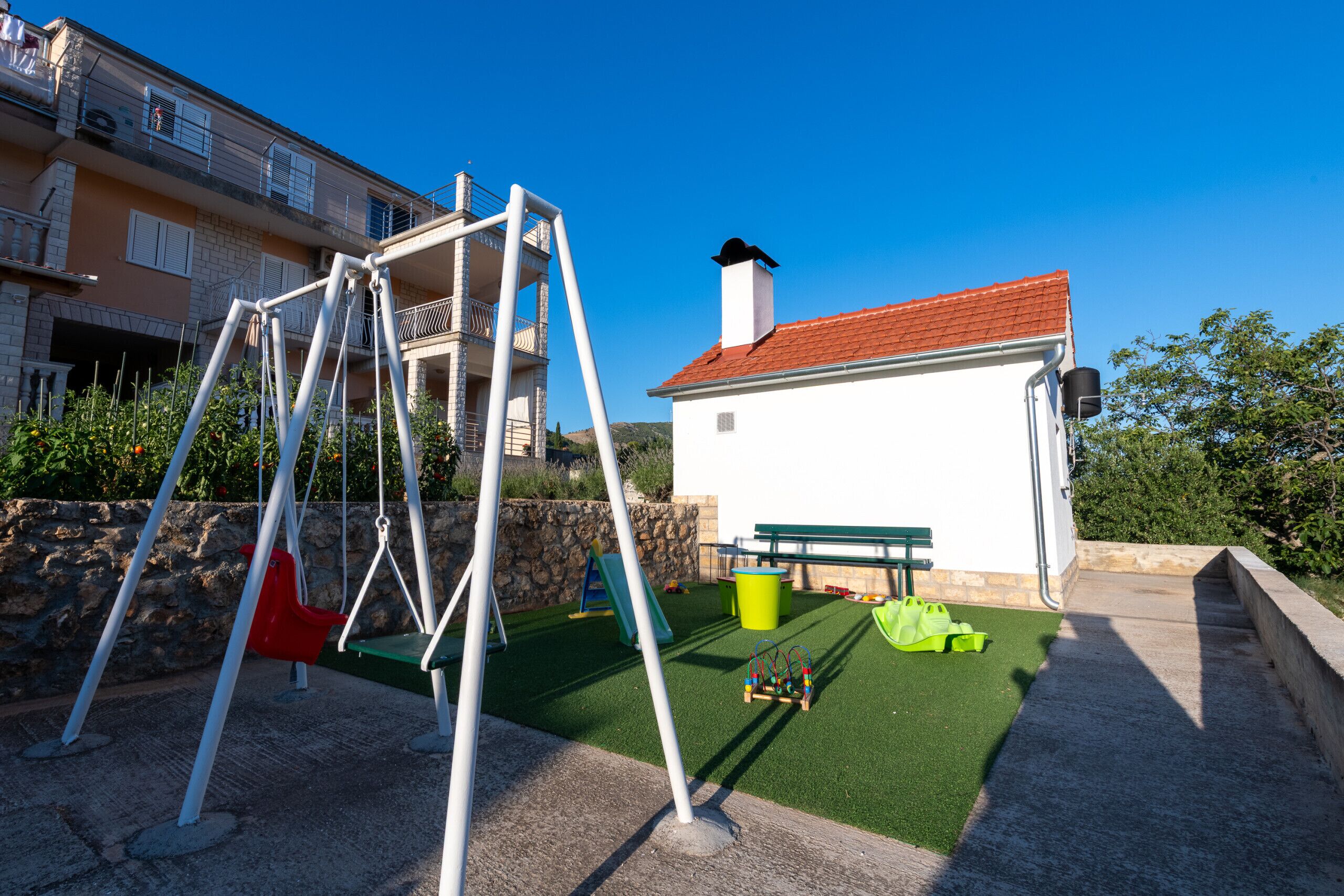 A playground with swings and a slide, a bench, and a small building with a red roof.