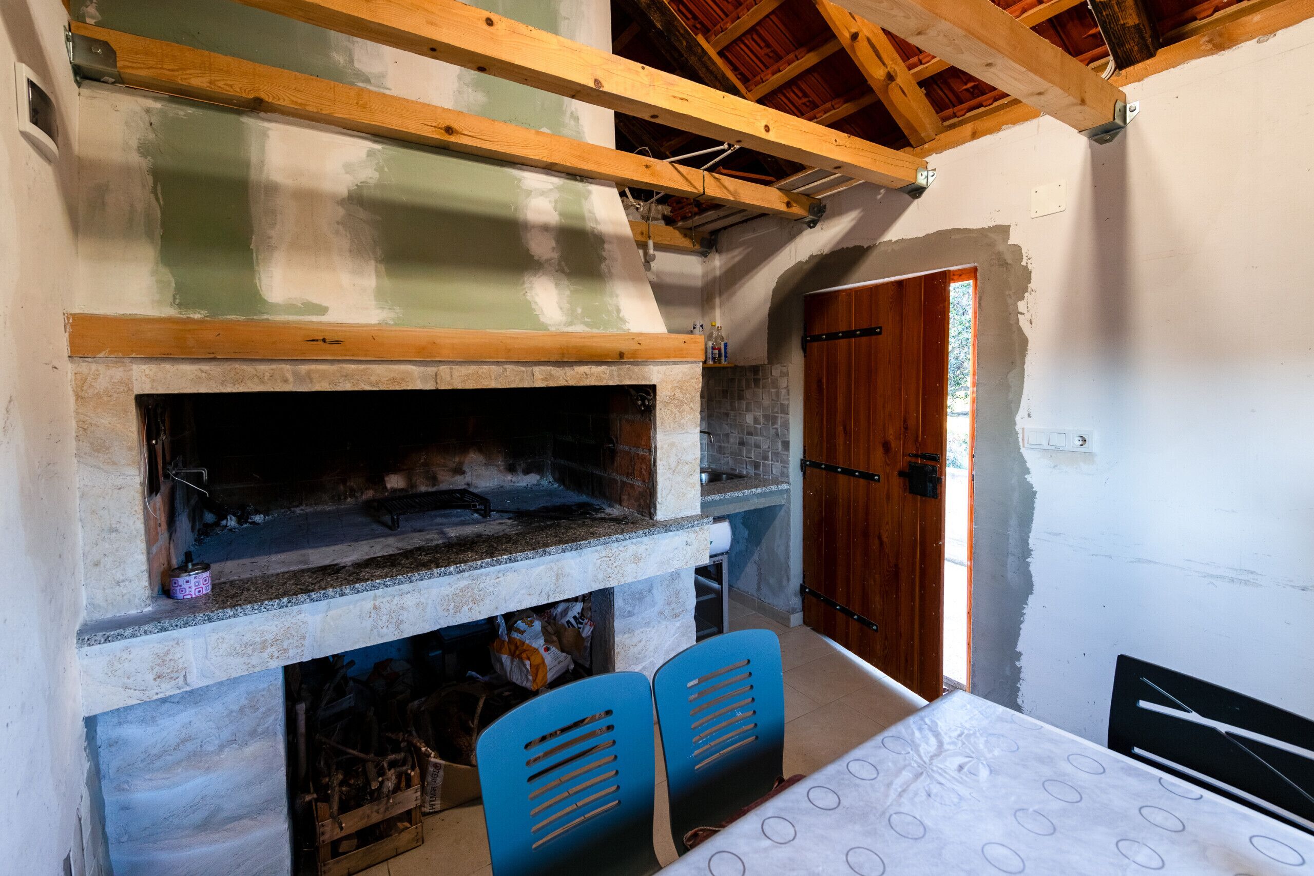 Una habitación con chimenea de piedra, vigas de madera, una puerta y sillas azules.