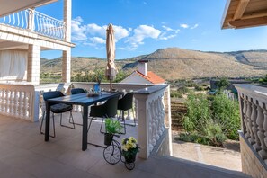 A balcony with a table and chairs, a potted plant, and a view of a mountainous landscape.