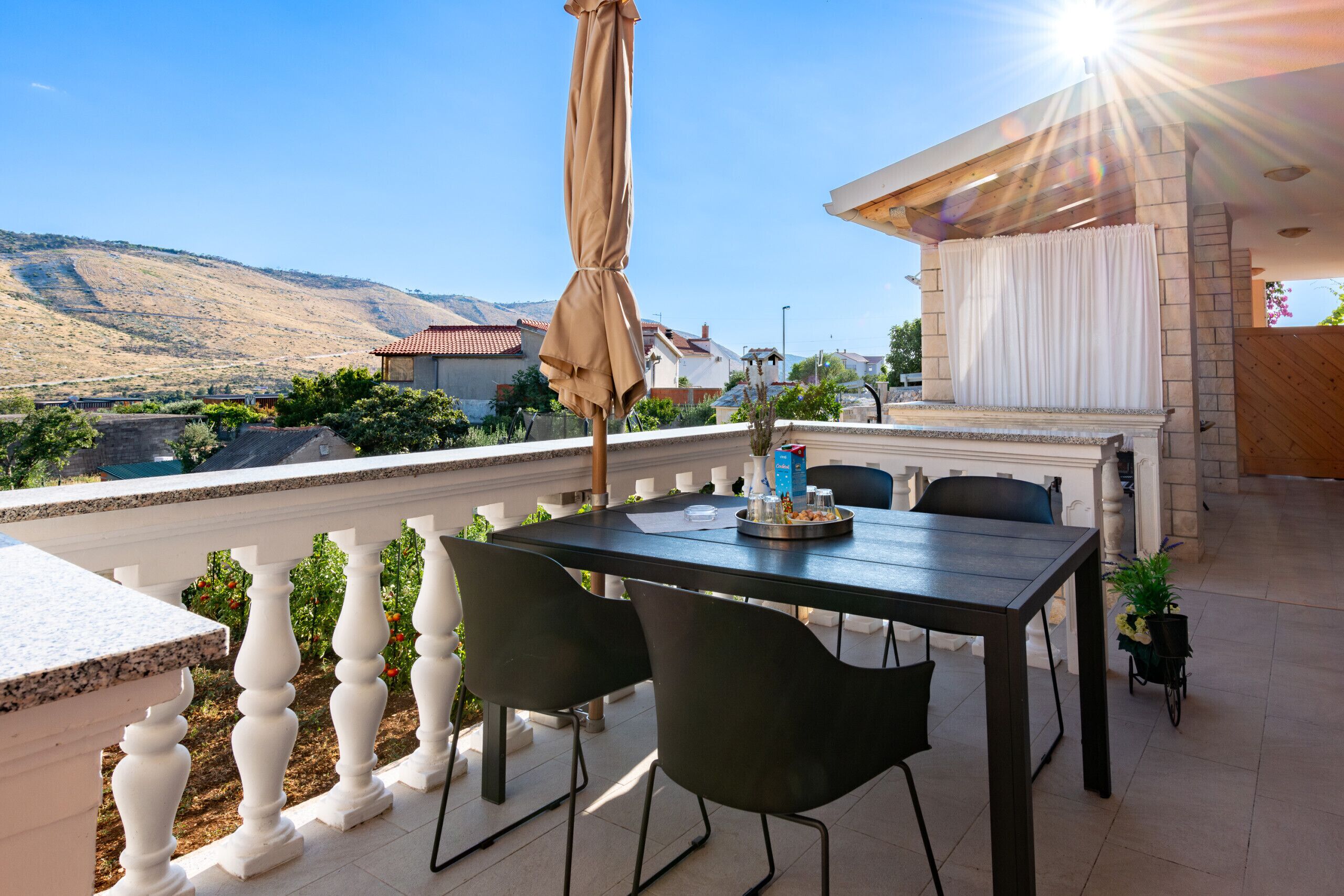 A terrace with a table and chairs, a barbecue area, and a view of a hilly landscape.