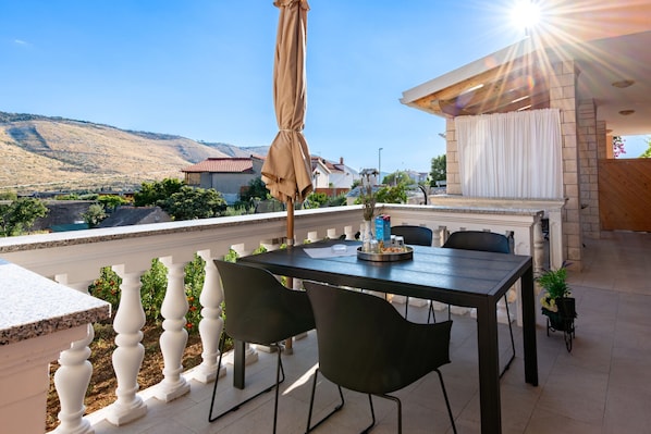 A terrace with a table and chairs, a barbecue area, and a view of a hilly landscape.