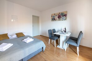A bedroom with a bed, two chairs, a table, and a painting on the wall.