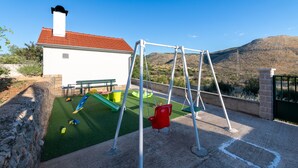 A patio with a swing set, a green play area, and a white building with a red roof.