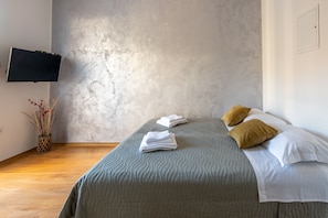A neatly made bed with a grey quilt, two pillows, and a folded towel.