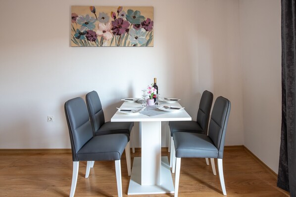 Un comedor con una mesa blanca, cuatro sillas grises y un cuadro floral en la pared.