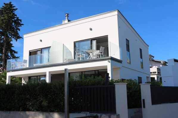 A modern two-story house with a balcony, large windows, and a flat roof.