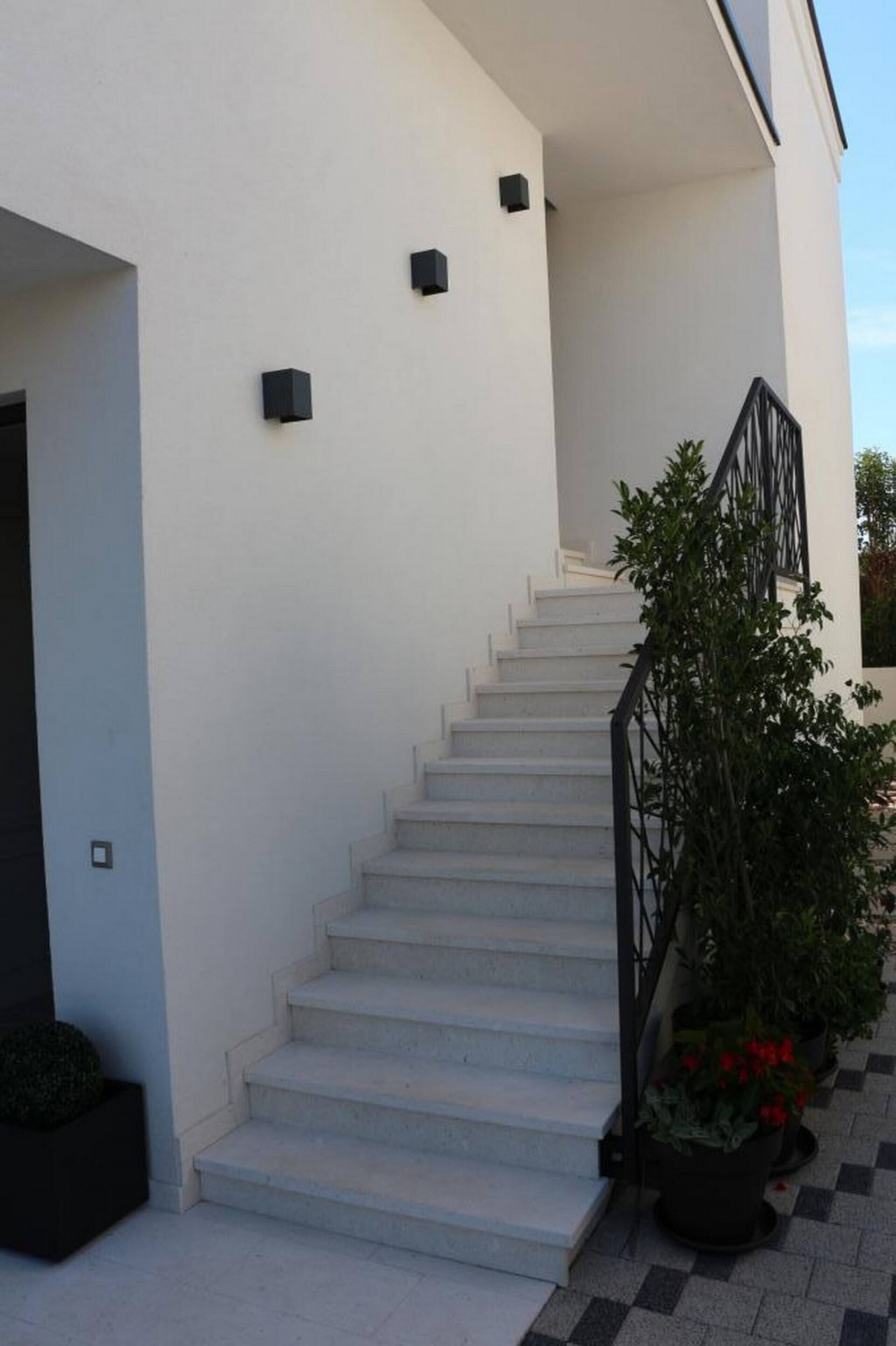 A staircase leading to a white building with black railings and potted plants.
