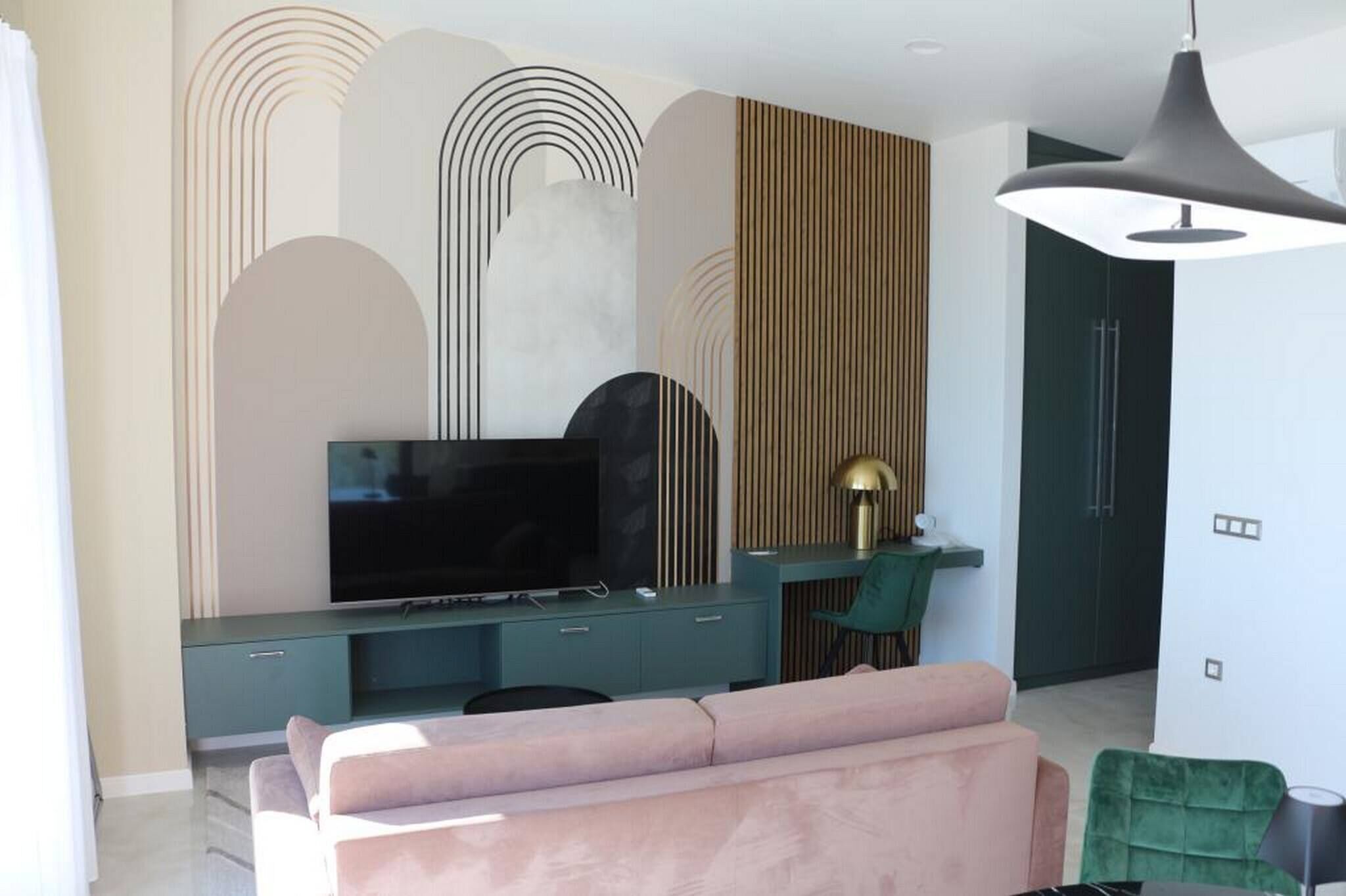 A modern living room with a large flat-screen TV, teal entertainment unit, and a green chair.
