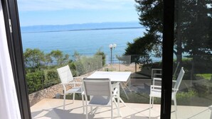 A balcony with a table and chairs, overlooking a body of water and greenery.