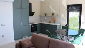 A modern kitchen with grey cabinets, a black stove, and a glass dining table with green chairs.