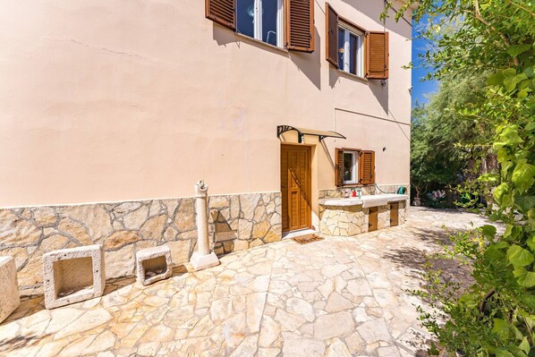 A stone-paved courtyard with a stone wall, wooden door, and window shutters. - Apartments Kukljica - one bedroom apartment with a sea view (Kukljica)