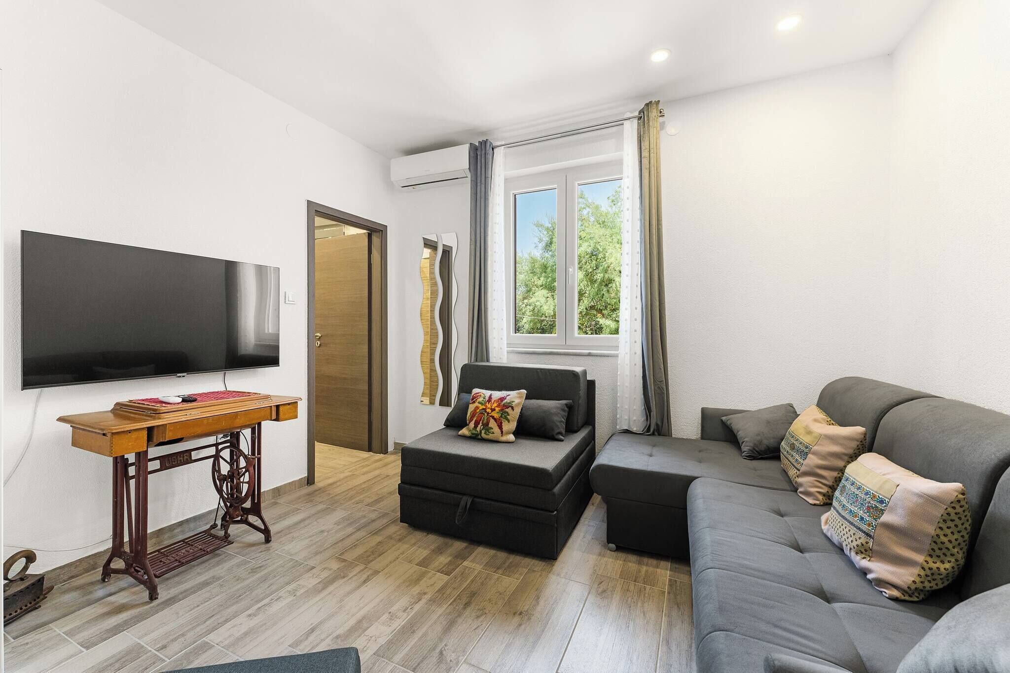 Ein modernes Wohnzimmer mit Flachbildfernseher, einem Holztisch, einer Couch und einem Fenster mit Vorhängen.